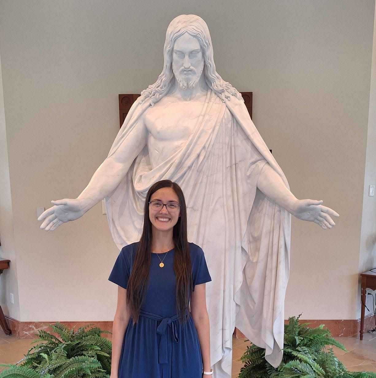 Rachel smiling in a navy dress in front of a white marble Christus statue with outstretched arms