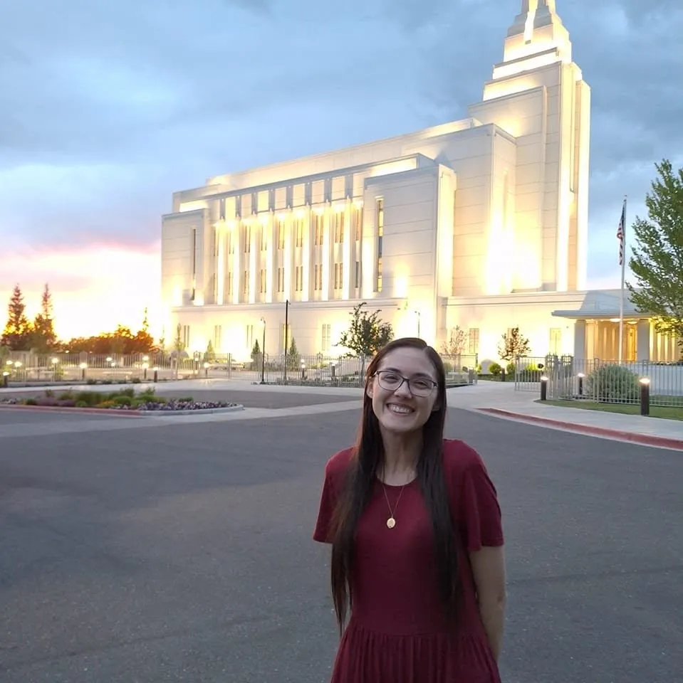 Rachel in a red dress standing in front of a white temple glowing at dusk