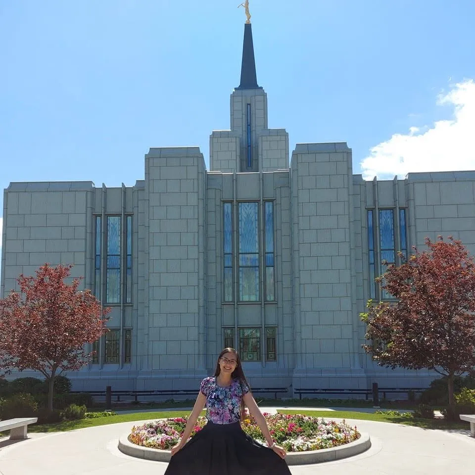 Rachel sitting by a round flower bed in front of a grey granite temple with a tall spire