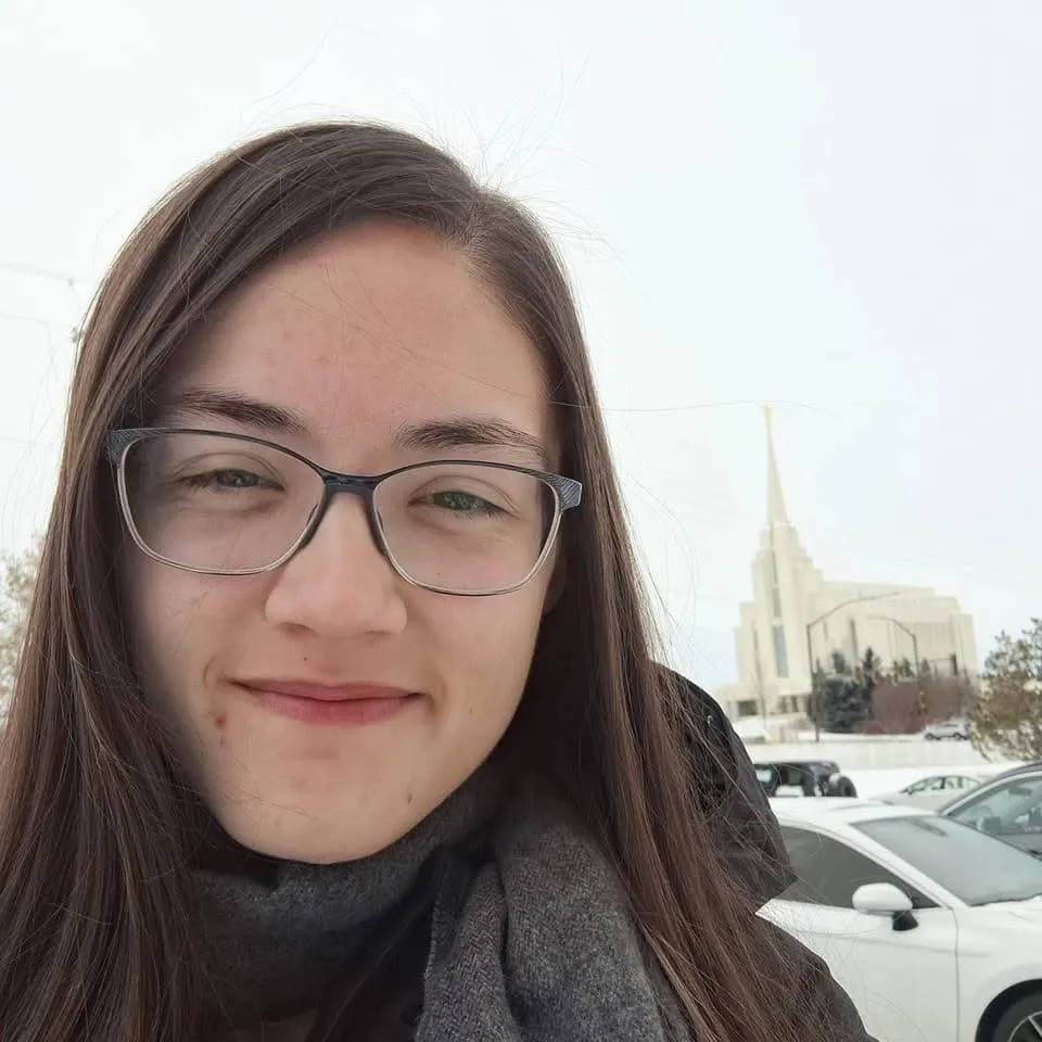 Close-up selfie of Rachel in a grey scarf on a wintry day, a white temple spire behind her
