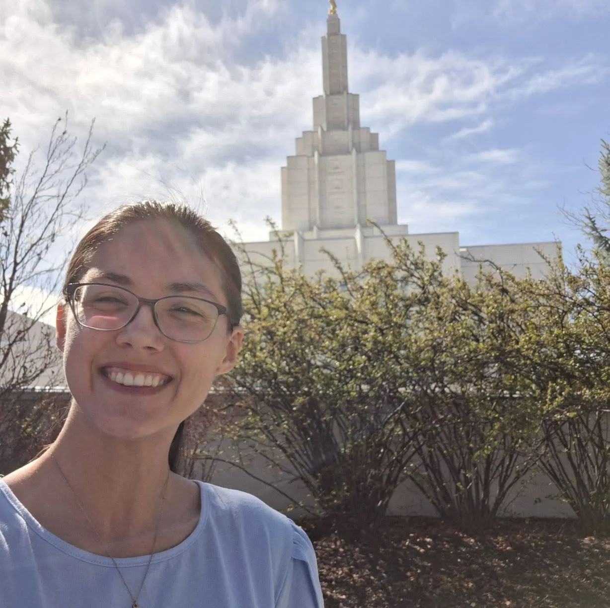 Rachel smiling in a selfie with the tall white spire of the Idaho Falls Idaho Temple behind her